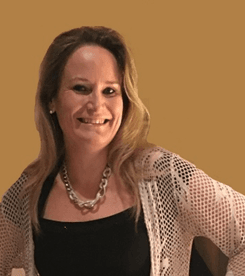 Das Foto wurde vor einer dunkelgelben Wand aufgenommen. Eveline Eppensteiner hat lange hellbraune Haare und trägt neben einem schwarzen T-Shirt eine helle Strickjacke und eine silberne Kette.