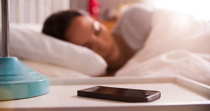 Eine schlafende Frau im Bett und im Vordergrund liegt ein Mobiltelefon auf dem Nachttisch Schrank .