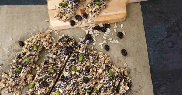 Auf Backpapier liegen mehrere Riegel aus Hafer, Sonnenblumenkernen und Cranberries.