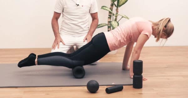 Patientin macht eine Faszien-Rollmassage mit der Maxi-Rolle von Liebscher & Bracht. Sie hat ihre Hände aufgestützt und ihre Beine auf Kniehöhe auf der Maxi-Rolle abgelegt.