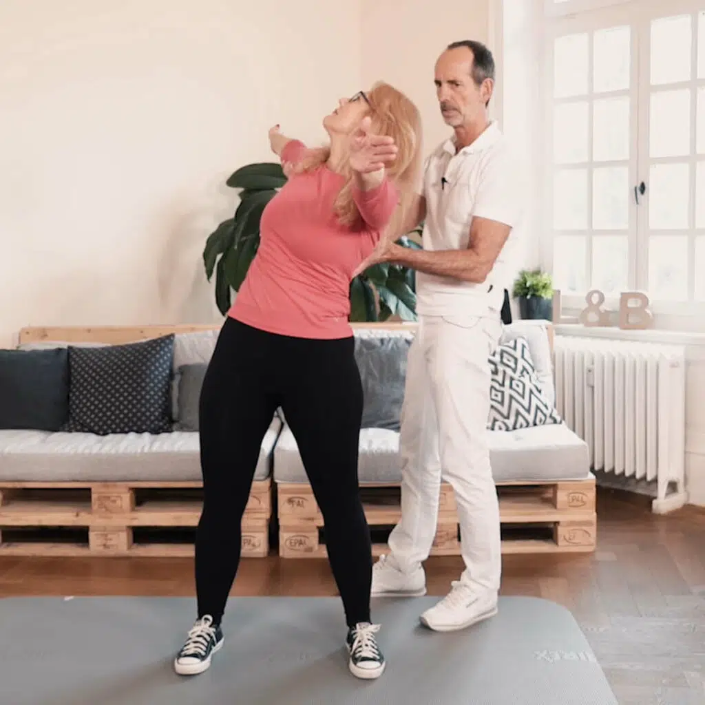 Eine Frau macht eine Rotationsübung, indem sie hüftbreit stehend den rechten Arm parallel zum Boden nach hinten ausstreckt, der linke Arm ist nach vorne gestreckt.