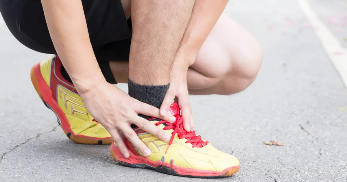 Ein Mann in Sportkleidung greift sich in der Hocke an seinen Fuß.