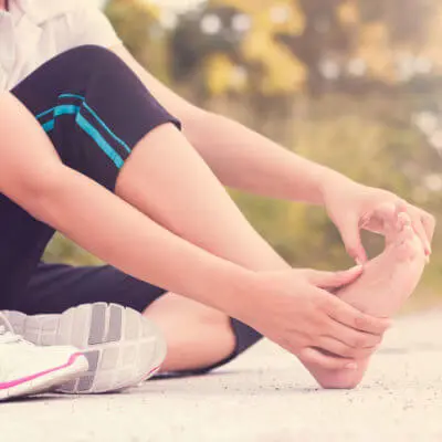 Frau hält sich nach dem Joggen den schmerzenden Fuß