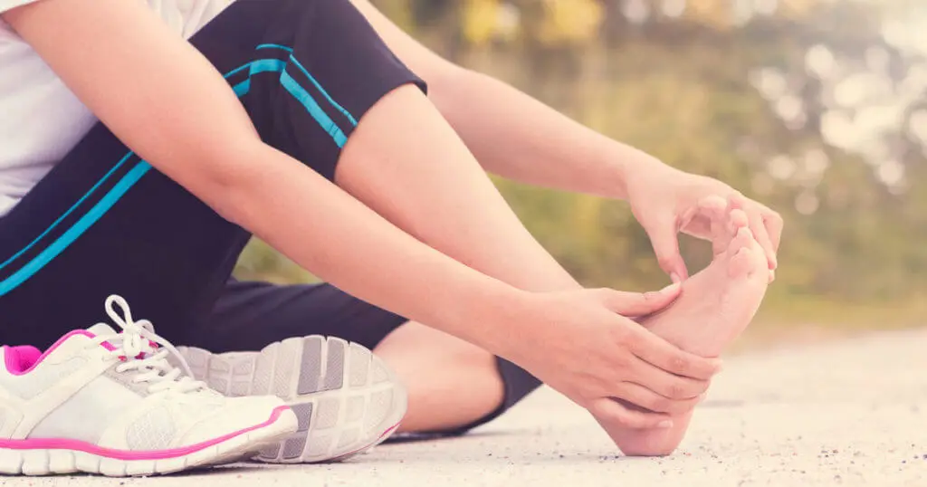 Frau hält sich nach dem Joggen den schmerzenden Fuß