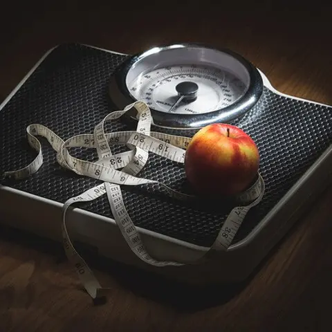 Ein Maßband und ein Apfel liegen auf einer Waage.