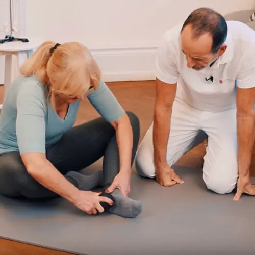 Faszien-Rollmassage mit der Mini-Kugel bei Hammerzehen, Haglundferse und Fersenschmerzen und Plantarfasziitis. Frau rollt sprialförmig mit der Mini-Kugel über die verspannten Stellen an der Fußsohle.