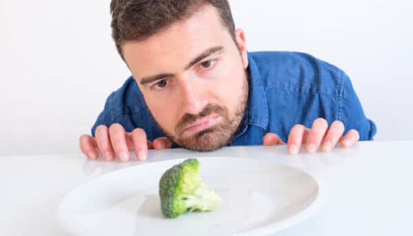 Ein Mann betrachtet traurig ein Brokkoli-Röschen auf einem Teller