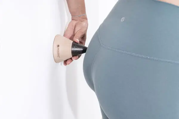 Eine Frauenhand hält den "Drücker" mit der flachen Seite an die Wand und mit der Spitze drückt sie sich einen Punkt seitlich am Po