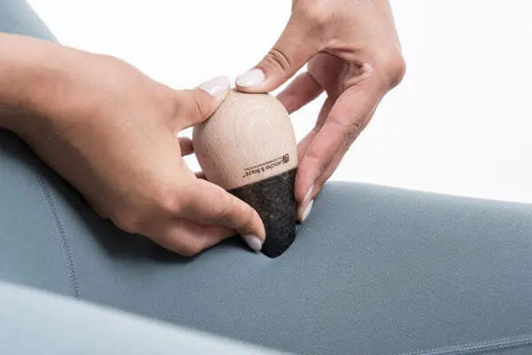 Zwei Frauenhände drücken den "Drücker" mit der Spitze in den Oberschenkel, der von einer Blauen engen Stoffhose umgeben ist.