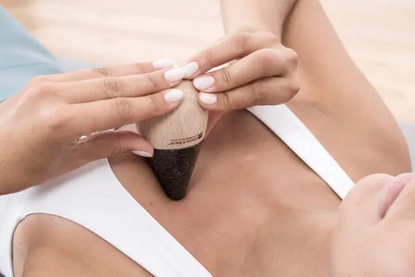 Zwei Frauenhände drücken den "Drücker" mit der Spitze sich einen Punkt kurz oberhalb der Brust einer liegenden Frau