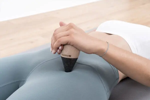 Zwei Frauenhände drücken fest den "Drücker" mit der Spitze in einen Punkt vorne auf der Hüfte einer liegenden Frau