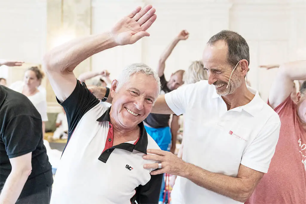 Mann dehnt sich nach Anleitung von Roland Liebscher Bracht und lächelt dabei in die Kamera