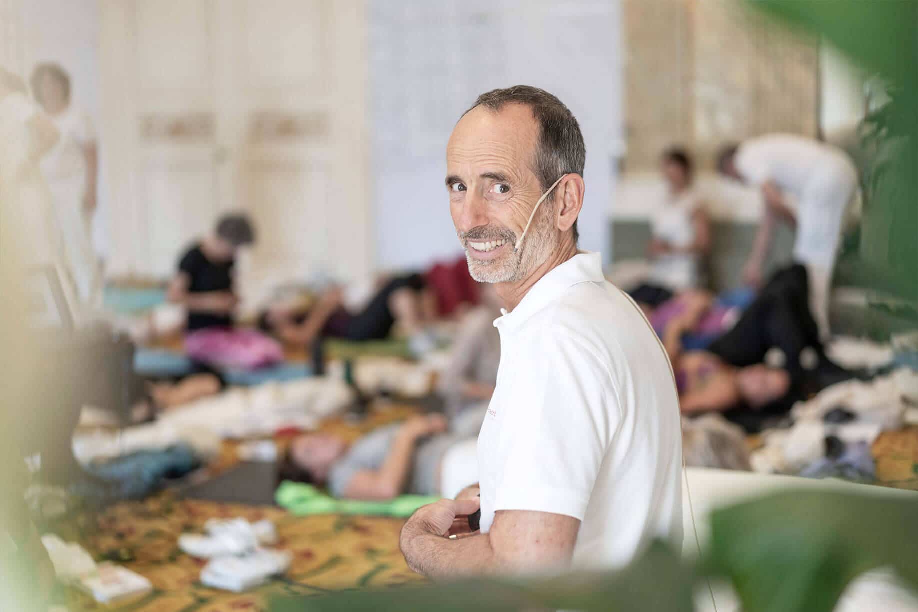 Roland Liebscher & Bracht hat sich umgedreht, um in die Kamera zu lächeln. Im Hintergrund liegen Teilnehmer der Ausbildung