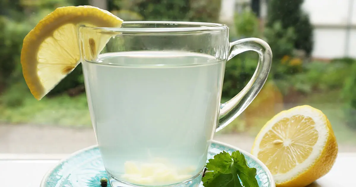 Ein Anti-Arthrose-Tee mit Ingwer, Kurkuma und Zitrone ist in einem Glas angerichtet. Eine halbe Zitrone liegt daneben und eine Scheibe ist am Glasrand angebracht.