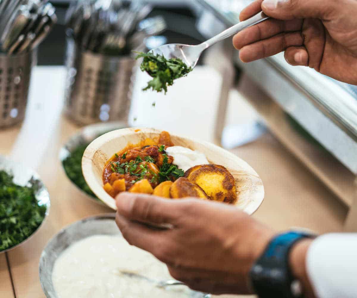 Der Koch teilt das Essen aus und verfeinert es mit frischen Kräutern