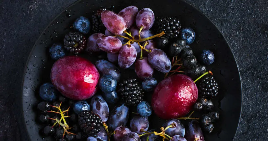 Beeren, Trauben und Pflaumen in einer schwarzen Schale.