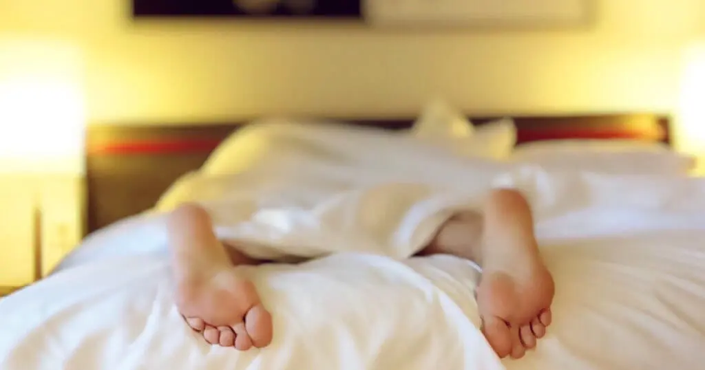 Frau liegt im Bett, die Füße schauen raus