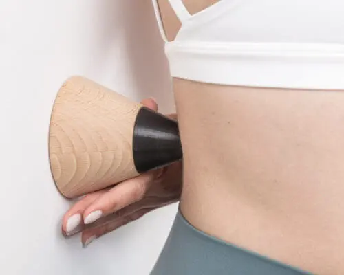 Anwendung des Schmerzfrei-Drückers an der Wand. Eine Patientin drückt einen Knochenpunkt am Rücken.