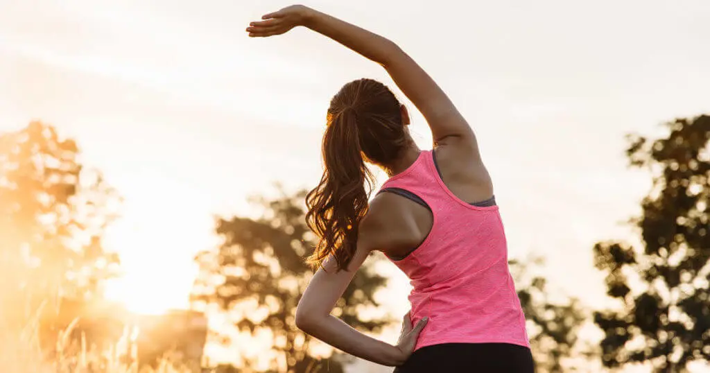 Eine junge Frau steht bei Sonnenaufgang in einem Park und streckt sich