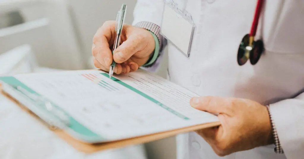 Ein Arzt hält ein Aktenbrett in der Hand und notiert sich etwas