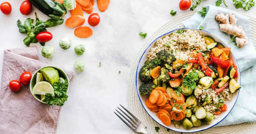 Eine Gemüsebowl steht auf dem Tisch, Gemüse liegt auch drumherum.