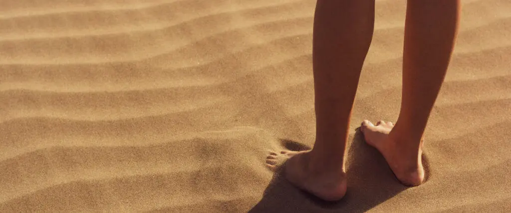 Nackte Füße stehen im trockenen Sand.
