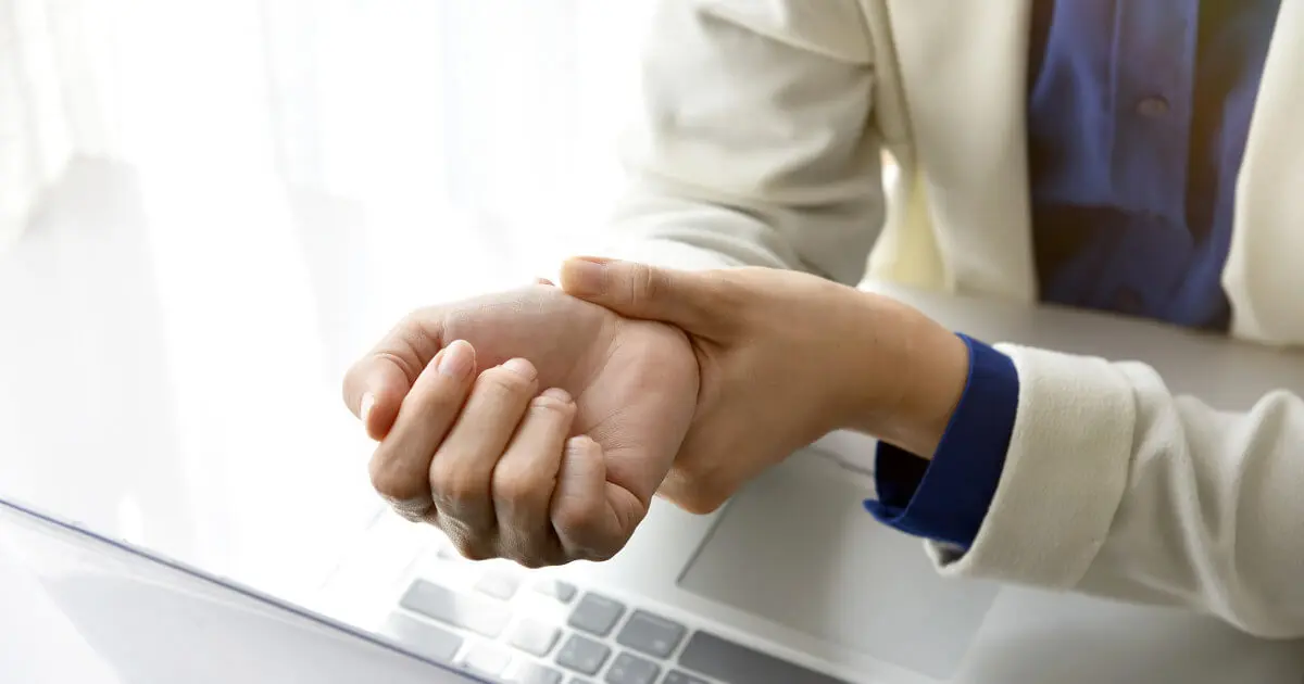 Eine Frau im Büro hält sich ihr Handgelenk vor Schmerzen aufgrund eines Karpaltunnelsyndroms