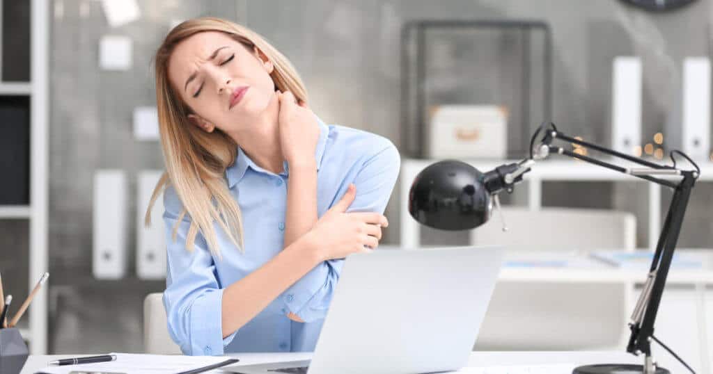 Eine junge Frau sitzt im Büro und hält sich vor Schmerzen ihren Nacken