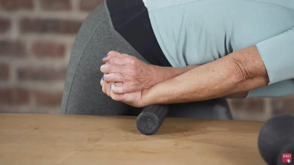 Eine Frau rollt ihr Handgelenk über die Mini-Faszienrolle und hält ihre Hand mit der anderen Hand fest., wobei sie die Finger nach oben dehnt
