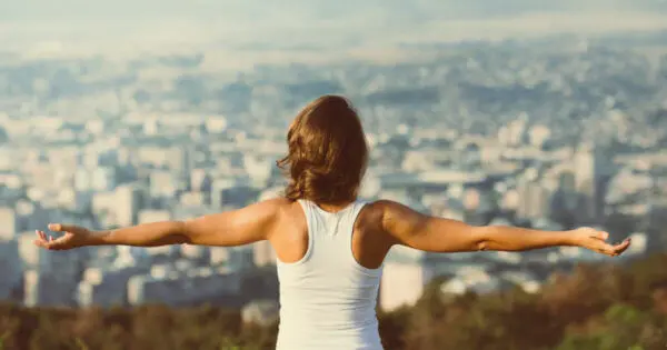 Eine Frau steht mit ausgestreckten Armen da, der Rücken ist zur Kamera gewandt. Sie blickt in die Ferne über eine große Stadt.