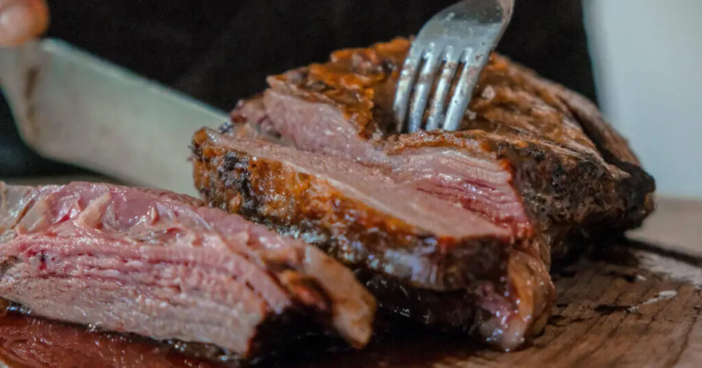 Ein großes Stück Fleisch liegt auf einem Holzbrett und wird angeschnitten