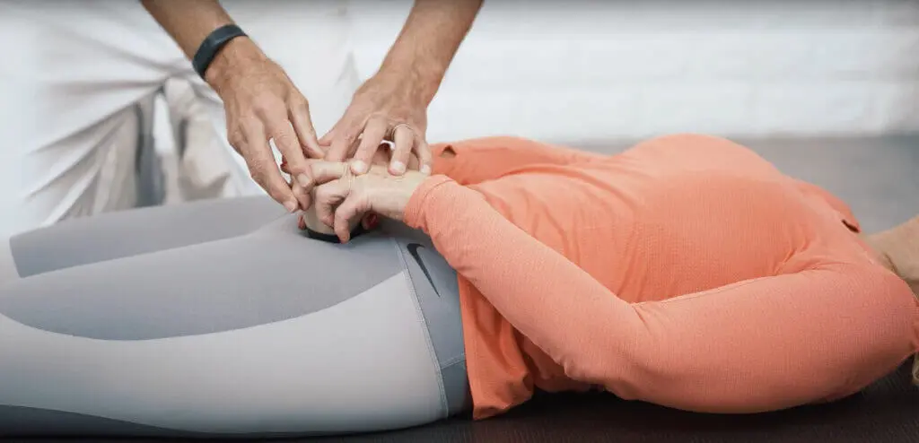 Eine Frau liegt auf dem Rücken und drückt den Schmerzfrei-Drücker von Liebscher & Bracht auf einen Knochenpunkt in der Nähe des Hüftstachels