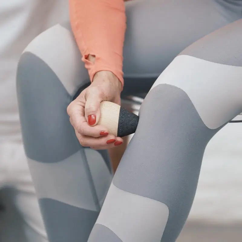 Eine Frau behandelt ihr Knie mit einem Drücker von Liebscher & Bracht und einer Light-Osteopressur, indem sie damit einen Punkt an ihrem linken Knie drückt.