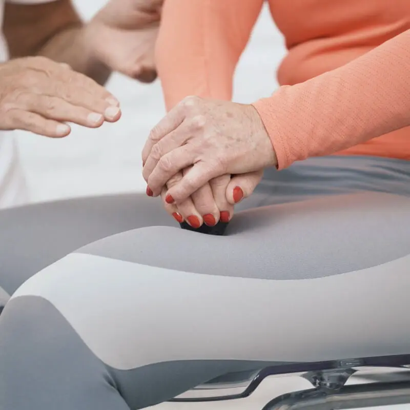 Eine Frau behandelt mit dem Schmerzfrei-Drücker von Liebscher & Bracht ihre Knieschmerzen, indem sie die Rundspitze auf ihren Oberschenkel-Knochen drückt.