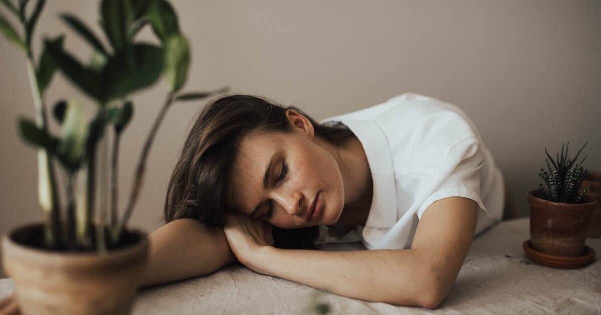 Eine Frau sitzt am Schreibtisch und legt vor Erschöpfung ihren Kopf auf dem Tisch ab
