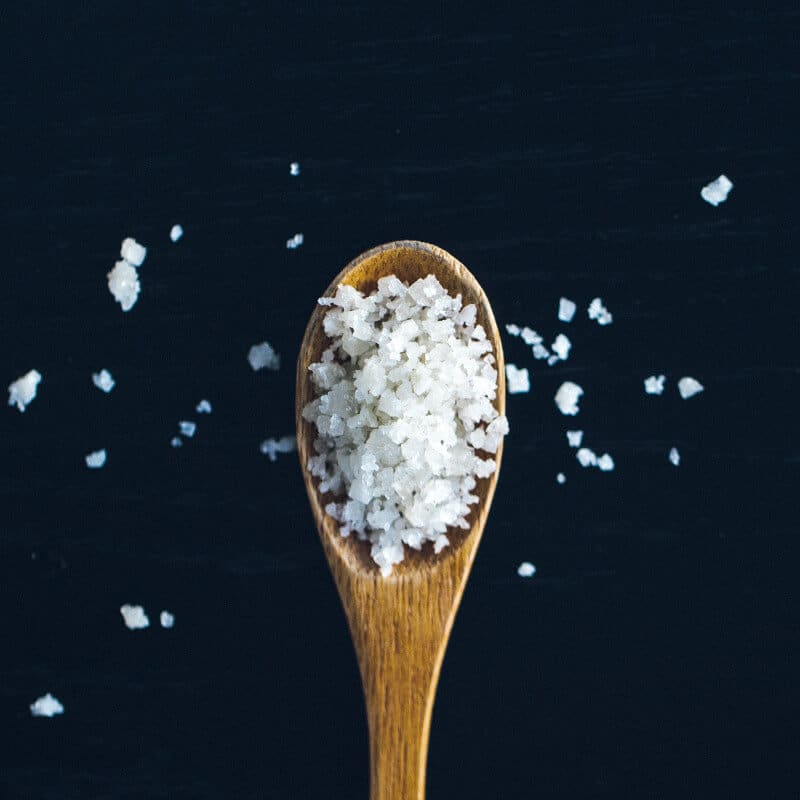 Ein Holzlöffel voller Salzkörner auf dunkelblauem Hintergrund