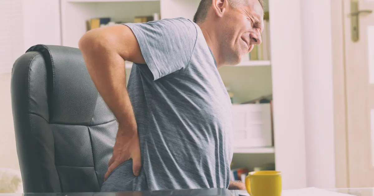 Mann sitzt auf einem Buerostuhl und hält sich seine schmerzende Lendenwirbelsäule