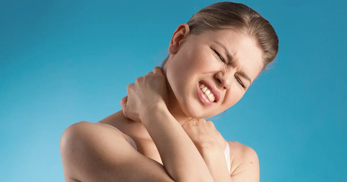 Eine junge Frau hält sich mit schmerzverzerrtem Gesicht den Nacken.