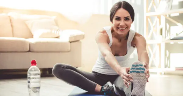 Eine Frau in Sportkleidung sitzt aufrecht auf einer Übungsmatte und beugt sich nach vorne zum linken ausgestreckten Bein. Das rechte Bein ist angewinkelt
