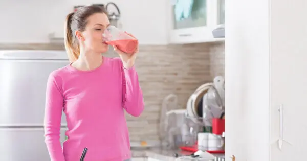 Eine Frau steht in ihrer Küche und trinkt einen Beeren-Smoothie