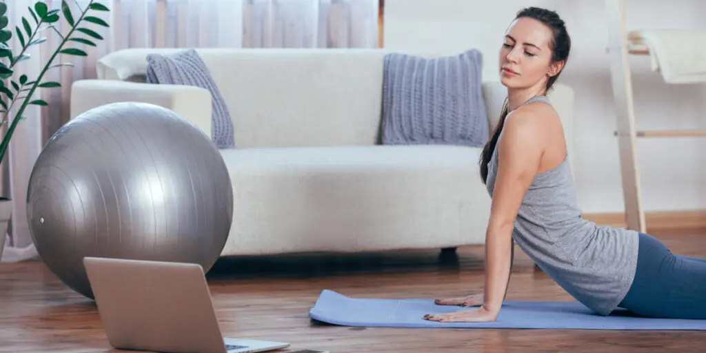 Eine junge Frau sitzt auf ihrer Matte und macht zuhause Online-Übungen