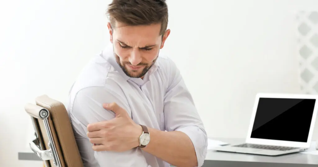 Ein Mann hält sich im Büro seine schmerzende Schulter