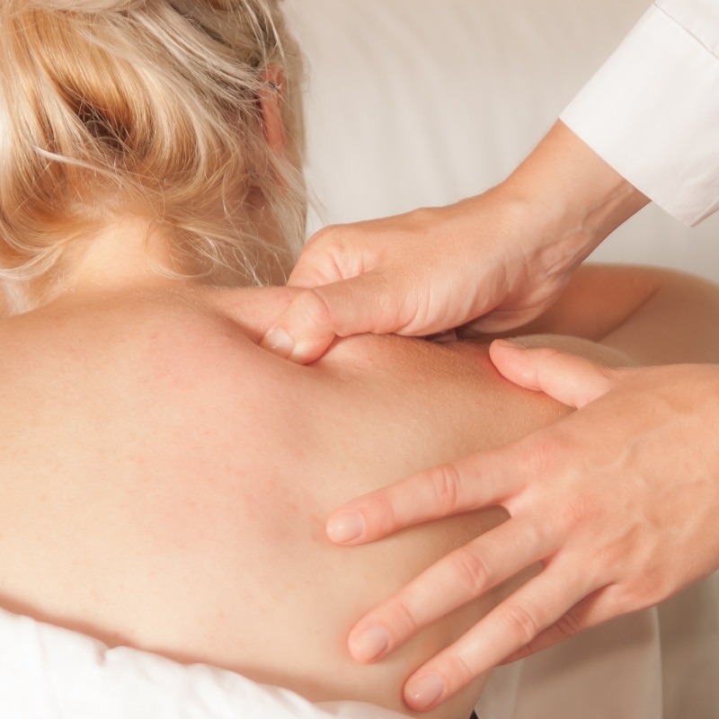 Eine Frau wird an der Schulter mit dem Daumen massiert als Triggerpunktmassage