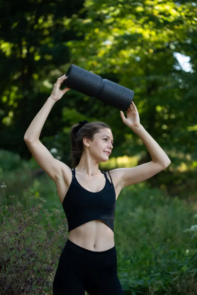 Frau steht auf einer Wiese in der freien Natur und hält eine Maxi Faszienrolle mit beiden Händen in die Höhe über ihren Kopf