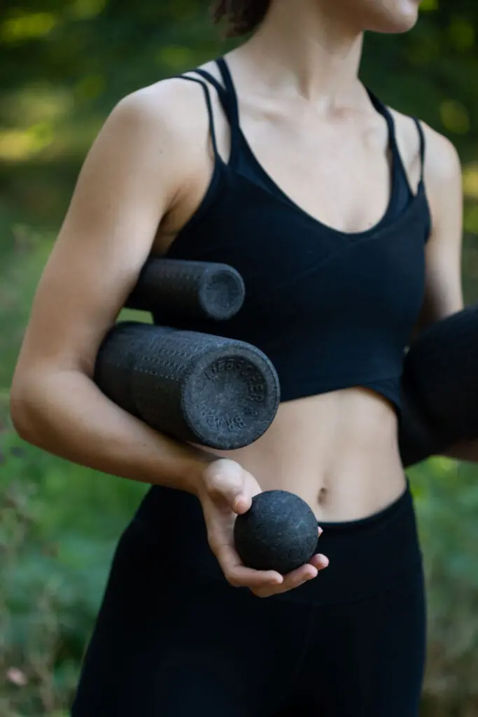 Frau steht in der freien Natur und hält verschiedene Faszienrollen und Faszienkugeln von Liebscher & Bracht