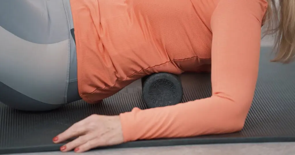 Eine Frau führt eine Faszien-Rollmassage am Rücken durch und verwendet dabei eine Rolle, die ihre Wirbelsäule schont
