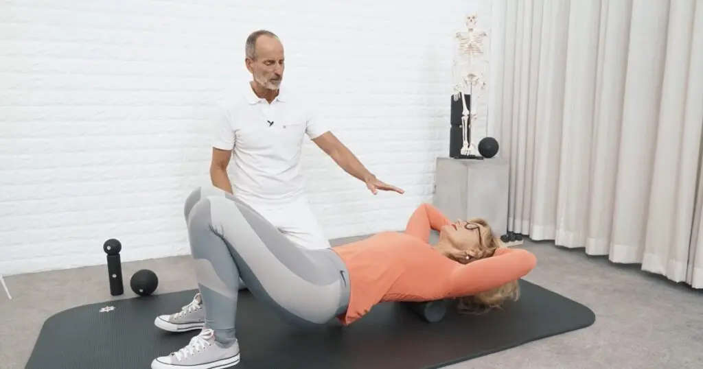 Roland Liebscher-Bracht weist eine Frau an, die eine Faszienrollmassage am Rücken macht.