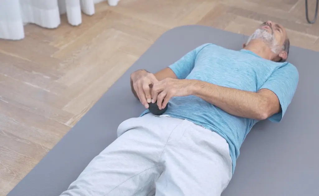 Mann rollt mit einem Faszienball entlang des Darmbeins, um Rückenschmerzen im unteren Rücken zu lindern