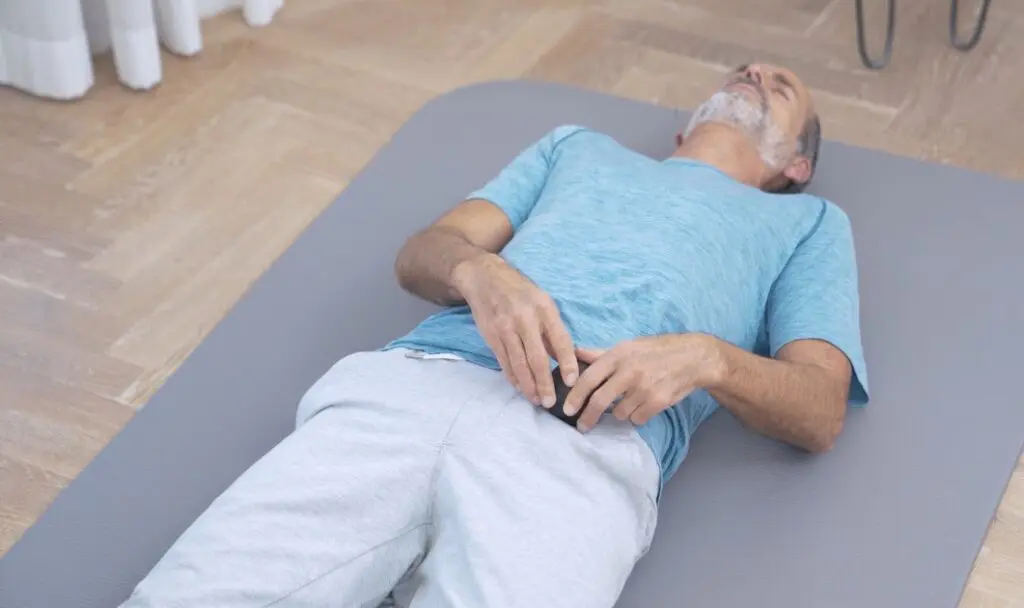 Roland Liebscher-Bracht liegt auf dem Rücken auf einer Übungsmatte und drückt die Mini-Kugel von Liebscher & Bracht in den Lendenbereich.