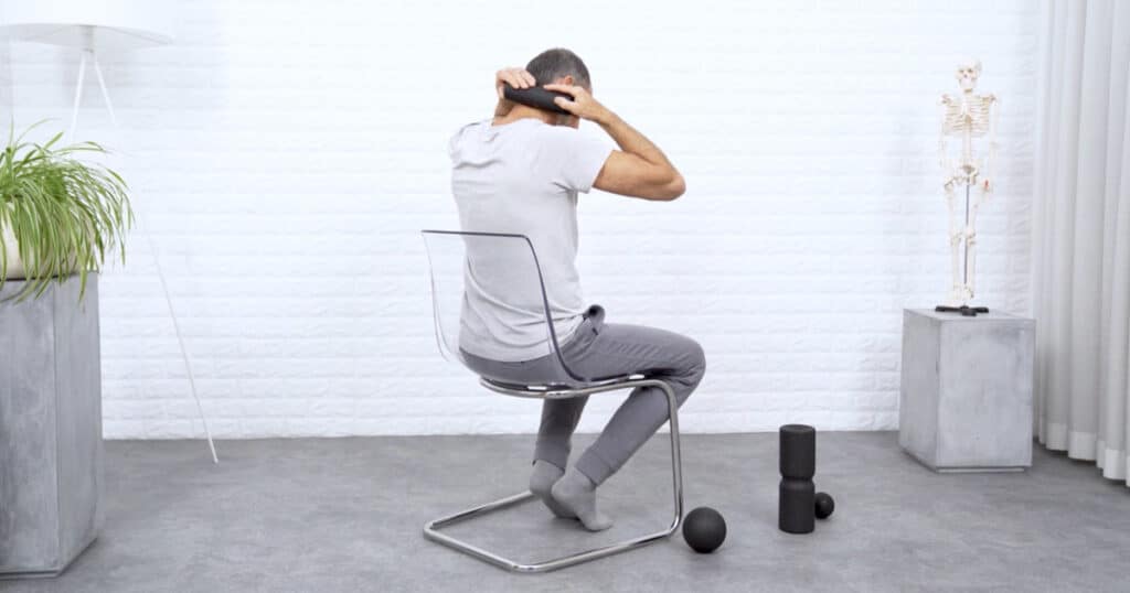 Ein Mann rollt mit einer kleinen Faszienrolle den Mittelteil des seitlichen Nackenbereichs ab